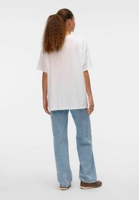 Camiseta blanca de gran tamaño con mangas cortas, combinada con vaqueros rectos de color azul claro y zapatos marrones, con una textura suave.