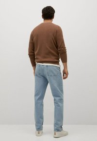 Brązowy sweter z okrągłym dekoltem, jasnoniebieskie dżinsy i beżowe trampki. Tkanina wydaje się miękka, o luźnym kroju i minimalnych zdobieniach.