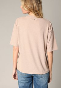 Haut beige à rayures, à manches courtes, avec un col rond, présentant un petit détail de bouton à l'arrière et une coupe décontractée. Tissu texturé.