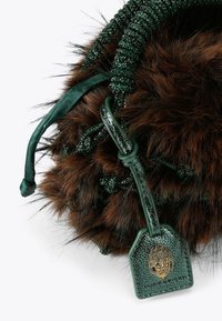 Borsa in pelliccia sintetica marrone con manico in tessuto verde e decorazioni. Presenta un'etichetta verde testurizzata con un dettaglio dorato.