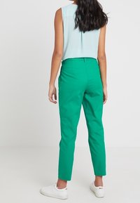 Pantalones verdes ajustados con una textura suave, de corte slim y longitud cropped; combinados con una blusa sin mangas de color azul claro y zapatillas blancas.