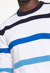 Stickad tröja med horisontella ränder i marinblått, mörkblått, ljusblått och vitt. Rundad halsringning med ribbad struktur.