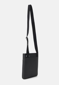 Borsa a spalla nera con una finitura liscia e texturizzata. Presenta una lunga tracolla regolabile e un design rettangolare minimalista.