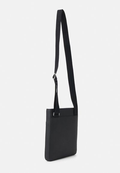 Sac à bandoulière noir avec une finition lisse et texturée. Dispose d'une longue sangle réglable et d'un design rectangulaire minimaliste.