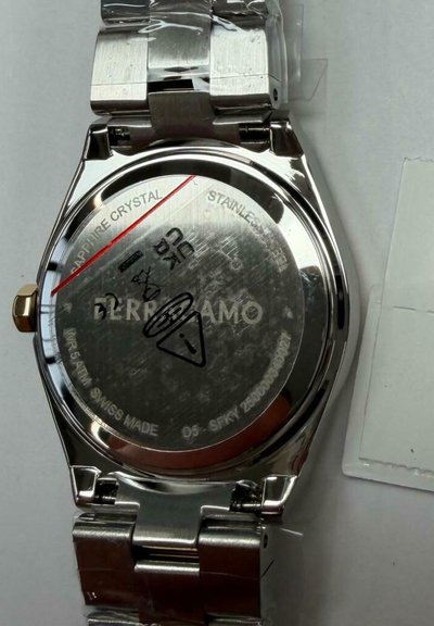 Achterkant van een roestvrijstalen polshorloge met merknaam, waterbestendigheid, saffierglas en gegraveerde waarschuwingssymbolen op een metalen armband.