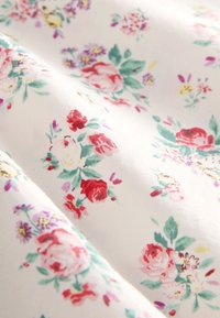 Țesătură albă cu un model de trandafiri grupați și flori mici în roșu, roz, mov și frunze verzi, ușor încrețită.