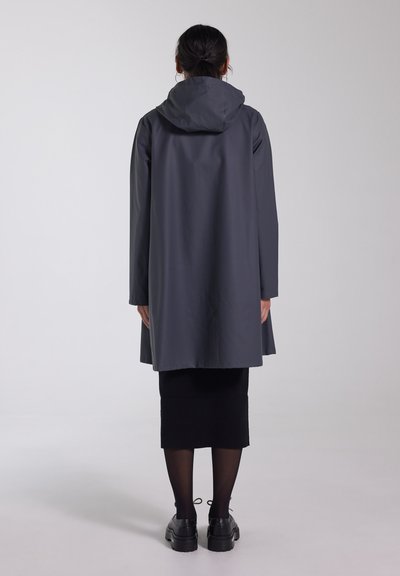 Grijze waterdichte jas met een capuchon, tot aan de knieën, met een gladde textuur, met een rechte snit en zonder zichtbare sluitingen. Gedragen over een zwarte rok.