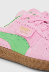 Sneaker Puma Palermo en daim rose avec une bande d'accent verte, des lacets roses, et une semelle texturée marron affichant le logo Puma sur le côté.