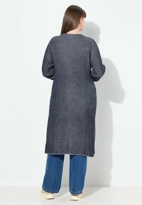 Neulepuuvilla, jossa on pystysuorat raidat, navy-sininen pitkä kardigan. Tässä on pyöreä kaulus ja kapeat hihat.