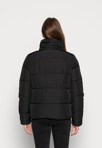 Czarna kurtka puchowa z wysokim kołnierzem, pikowanym wzorem oraz długimi rękawami. Posiada zamek błyskawiczny i luźny krój, prezentowana z widoku od tyłu.