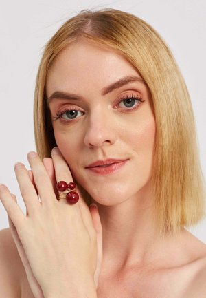 Red resin ring with three spherical beads, two larger and one smaller, mounted on a gold-colored band. Smooth texture and shiny finish.