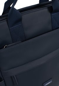 Marineblauwe tote bag met een gestructureerde buitenkant, stevige handvatten en zichtbare stiksels. Bevat een voorkantvak en een soepele ritssluiting.