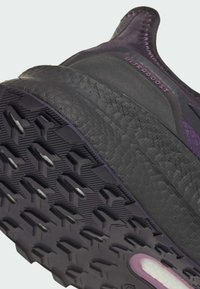 Semelle de chaussure de sport violet et noir avec un caoutchouc texturé, présentant un motif de traction et un marquage "ULTRABOOST" sur le côté.