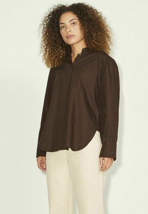 Chemise marron à manches longues en tissu lisse, dotée d'une poche poitrine unique et d'un ourlet arrondi, associée à un pantalon beige clair.