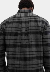 Grijze en zwarte geruite blouse, met een standaardkraag, lange mouwen en een textuurstof met opvallende patronen op de achterkant.