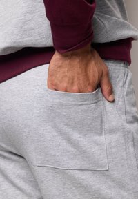 Pantalon de survêtement gris en coton avec une poche à rabat; associé à un t-shirt à manches longues bordeaux. Texture douce, design décontracté et coupe relaxée.