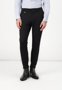 Crne slim-fit hlače s glatkom teksturom, s kopčanjem na dugme i bočnim džepovima. Uparene s crnim gležnjačama.