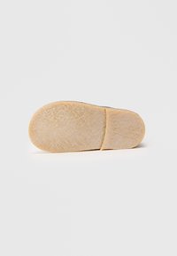 Suela de zapato con una superficie texturizada y parecida a la goma. El color es beige claro, con una forma suave y un patrón sutil para mejorar el agarre.