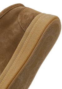 Brązowy zamszowy but z teksturowaną gumową podeszwą, z jasnym brzegiem i wzorzystą powierzchnią dla lepszej przyczepności.