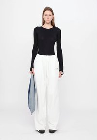 Black long-sleeve bodysuit paired with loose white trousers and a denim jacket draped over one arm. The outfit features a casual design.