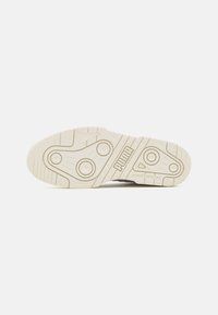 Semelle extérieure de basket Puma en caoutchouc beige avec motifs texturés antidérapants, deux accents circulaires et des détails en relief pour la traction.