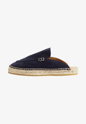 Zapato de ante azul marino tipo slip-on con una suela de yute trenzado. Presenta una parte superior curva y un pequeño detalle de hebilla metálica en el lateral. Interior con un forro suave.