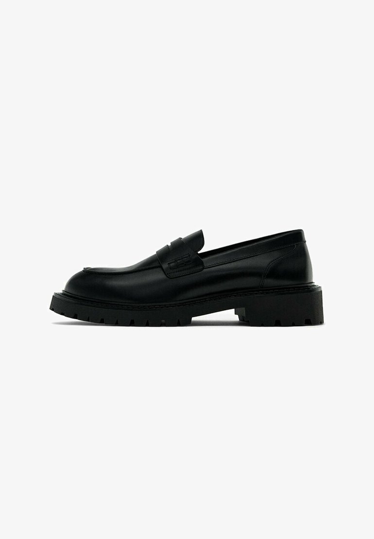 Mocassins en cuir noir avec une semelle épaisse et rainurée. Présentent une tige lisse, un accent cousu le long de l'avant-pied et une silhouette arrondie.