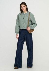 Veste bomber matelassée verte avec encolure ronde, associée à un jean denim foncé à jambes larges et un petit sac bandoulière marron.