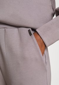 Jasnoszary sweatshirt z fakturowanej tkaniny, z boczną kieszenią i małą czarną metką na szwie. Miękki i casualowy design.