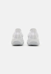 Et par hvide slip-on sneakers vist fra bagsiden med strukturerede gummisåler på en simpel hvid baggrund.