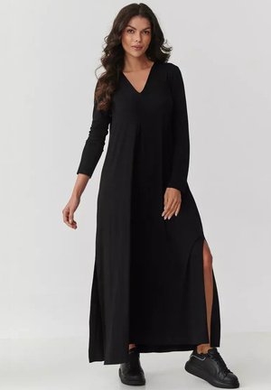 Czarna maxi sukienka z długimi rękawami, dekoltem w kształcie litery V, bocznymi rozcięciami i zwiewnym krojem. Noszona z czarnymi sneakersami, tworzy casualowy look.