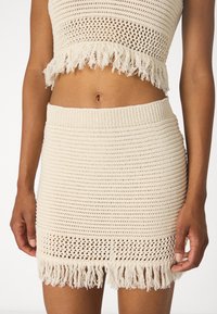 Strikket topp og skjørt sett i lys beige, med frynsekant og teksturerte mønstre, og en tettsittende design med ribbestrikket midjebånd.
