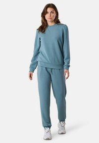 Maglione azzurro chiaro e pantaloni jogger coordinati in tessuto morbido. La felpa presenta un collo a giro e polsini a costine. I jogger hanno un elastico in vita.