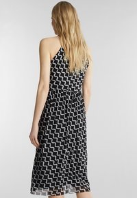 Robe à motif noir et blanc avec un décolleté halter et un dos nu, dotée d'une ceinture à la taille et d'un tissu fluide qui tombe jusqu'au mollet.