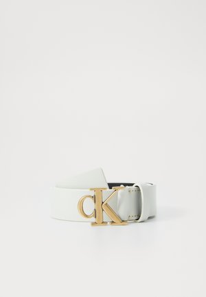 Witte leren riem met gouden metalen "cK" logo gesp, opgerold en geplaatst op een effen witte achtergrond.