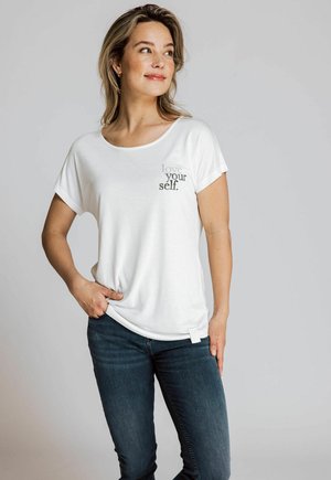 Weißes T-Shirt mit kurzen Ärmeln und dem Aufdruck "love your self." in Grau, lockere Passform, leichtes Material, kombiniert mit dunklen Skinny Jeans.