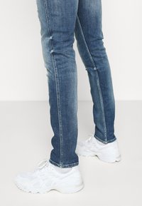 Bílé sportovní boty s detailním prodyšným materiálem a šněrováním, doplněné modrými džíny s slim fit střihem a vybledlým vzhledem.