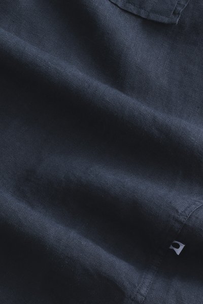 Navyblauwe linnen stof met een subtiele textuur, voorzien van een gevouwen hoek en een klein wit label nabij de naad.