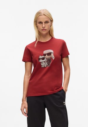 Red cotton T-shirt featuring a graphic of a character and a cat, both wearing sunglasses. The design is centered on the chest area.