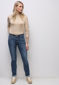 Vaaleanbeige istuva neule, siniset slim fit -farkut käännetyillä lahkeilla ja vaaleanbeige tennarit. Sileä tekstuuri, rento muotoilu, hienovaraiset yksityiskohdat taskuissa.