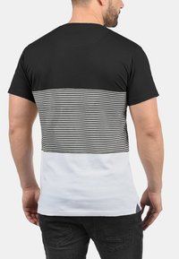Camiseta negra de manga corta con un patrón a rayas en la mitad superior y la mitad inferior en blanco sólido, hecha de tela suave.