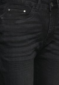 Pantalones vaqueros negros de mezclilla con una textura suave, diseño clásico, que cuentan con un pequeño bolsillo delantero y acentos de metal plateado.