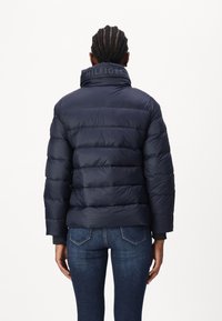 Giubbotto imbottito blu navy con imbottitura a segmenti, colletto alto e branding "HILFIGER" sul collo. Presenta polsini a coste e una vestibilità slim.