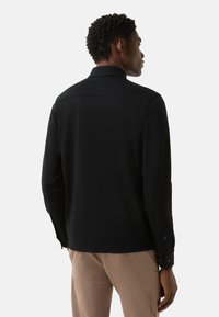 Schwarzes Langarmhemd mit strukturiertem Kragen, geknöpften Manschetten und glatter Textur. Sichtbare Nähte entlang der Schulternähte.