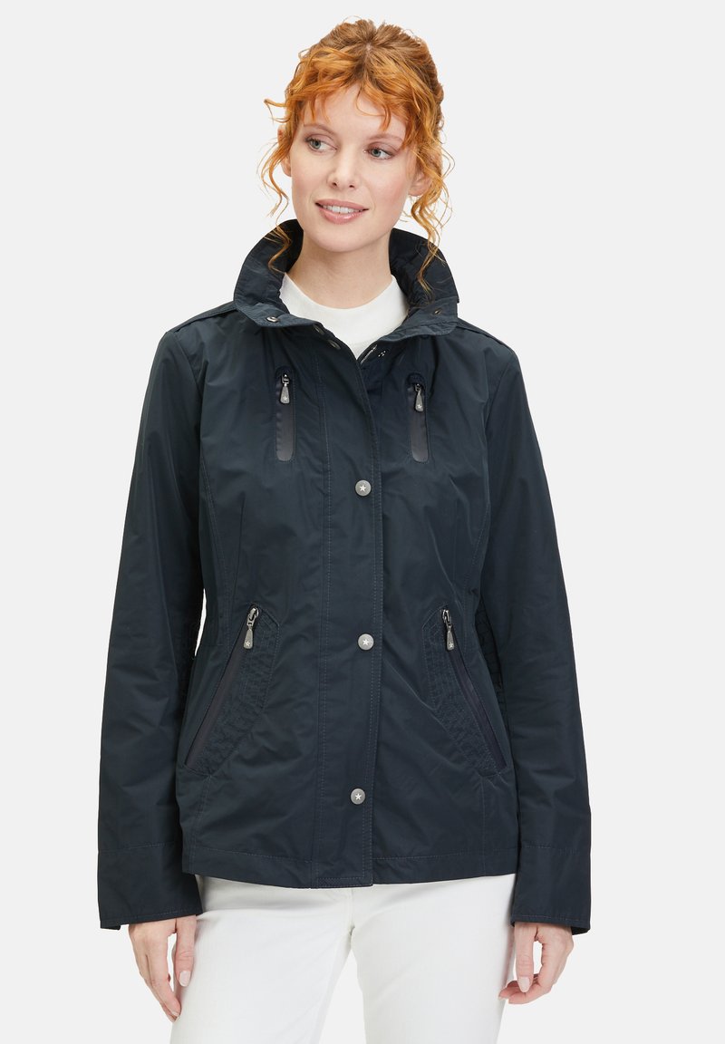 Dark navy waterproof jacket with a zippered front, multiple pockets, a high collar, and textured side panels. Smooth fabric finish.