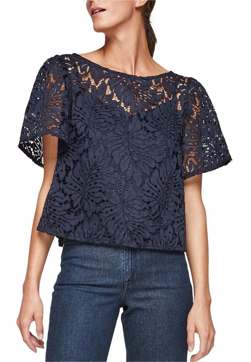 Débardeur en dentelle bleu marine avec des manches courtes et larges, arborant un motif floral et un col rond. Associé à un jean en denim ajusté.