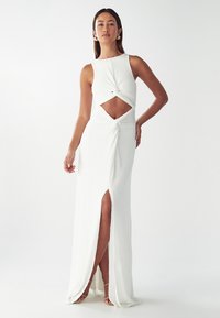 Vestido blanco con un diseño ajustado, que presenta un detalle de frente retorcido y una abertura lateral. La tela parece suave y fluida. Acentuado con un corte.