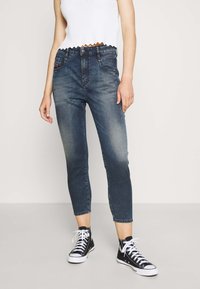 Jeans de denim de tiro alto, de lavado oscuro, con un ajuste slim, longitud recortada y detalles desgastados, combinados con zapatillas negras de caña alta.