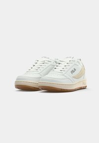 Hvite lær sneakers med teksturerte detaljer, beige gummisåle og hvite snøringer. Har perforeringer på tåen og en logo på siden.