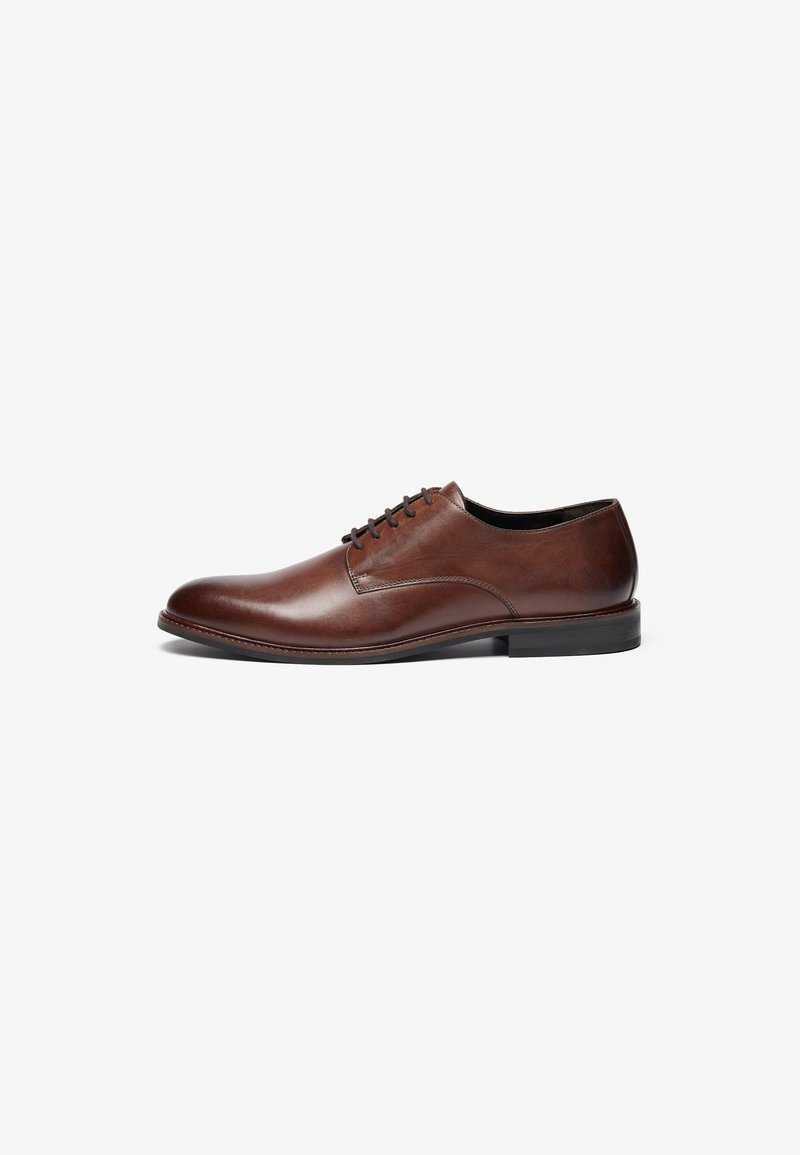 Scarpa elegante in pelle marrone con superficie liscia, punta rotonda e cinque occhielli per i lacci. Presenta un tacco nero basso e dettagli di cucitura minimalisti.